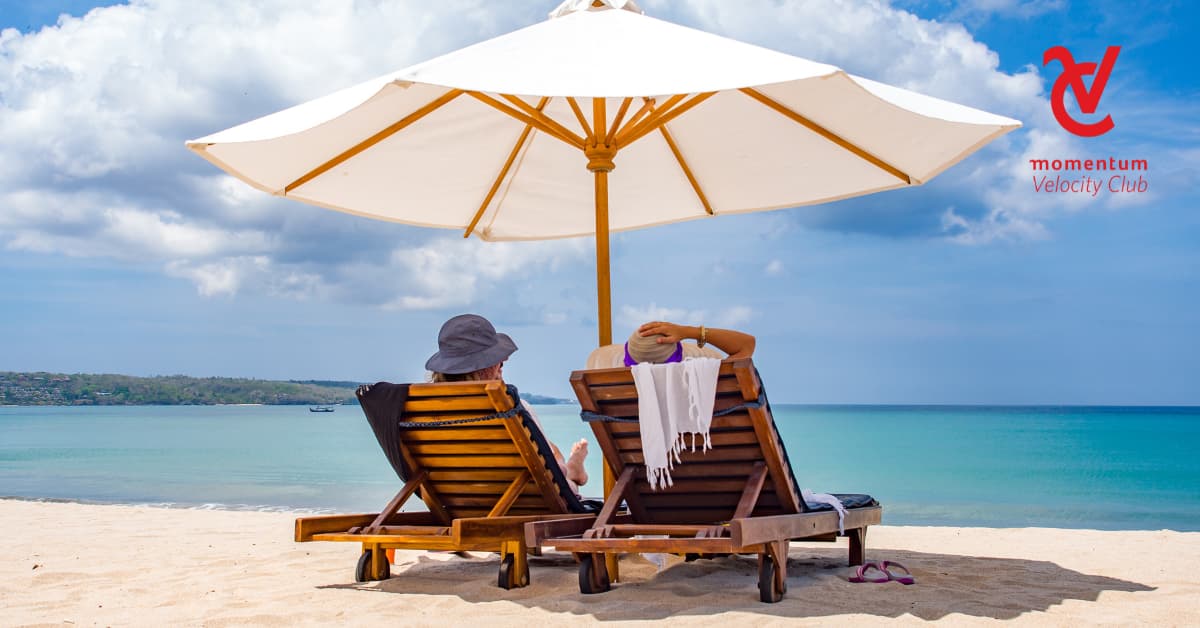 Two people are relaxing and sitting on wooden deck chairs by the sea.