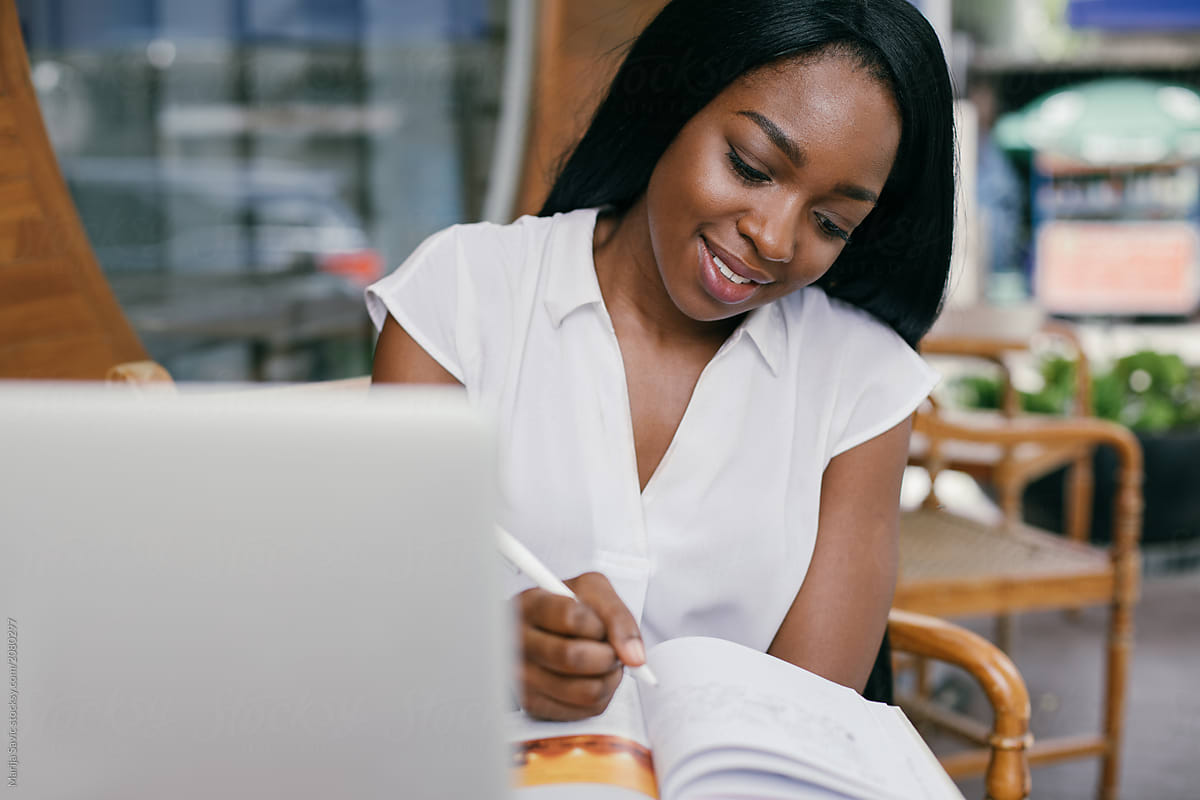 African lady dressed in a white shirt seated at a table jotting down her financial goals.