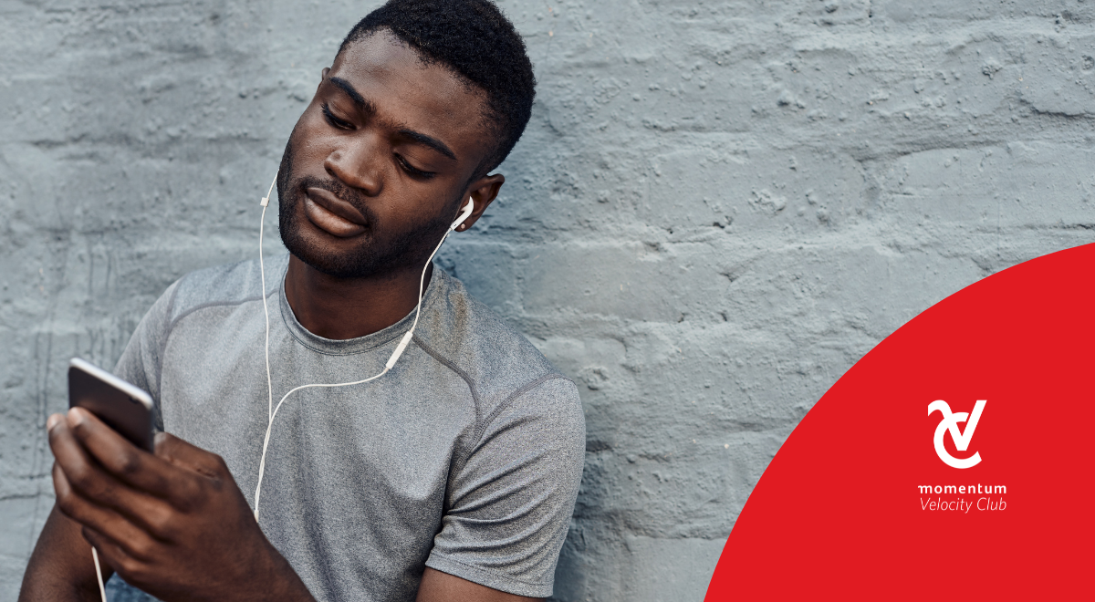 A young man with earphones listening to a financial podcast on his cell phone.