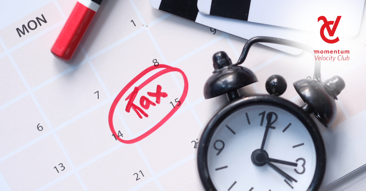 A desk calendar with the word 'Tax' written on one of the dates. On the desk calendar is a clock.