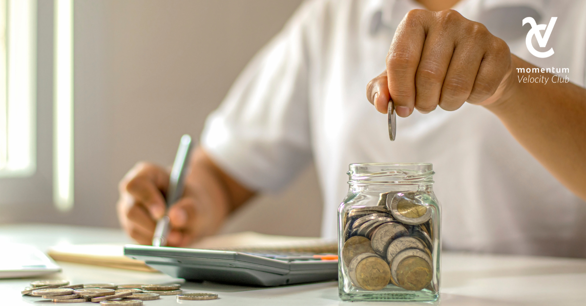 A person calculating their holiday budget with a calculator and putting coins in a jar as a means of saving.