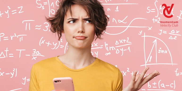 An image of a lady holding her cell phone; she's standing in front of a board and looking up. All the mathematical sums and equations written on a board behind her have her baffled.