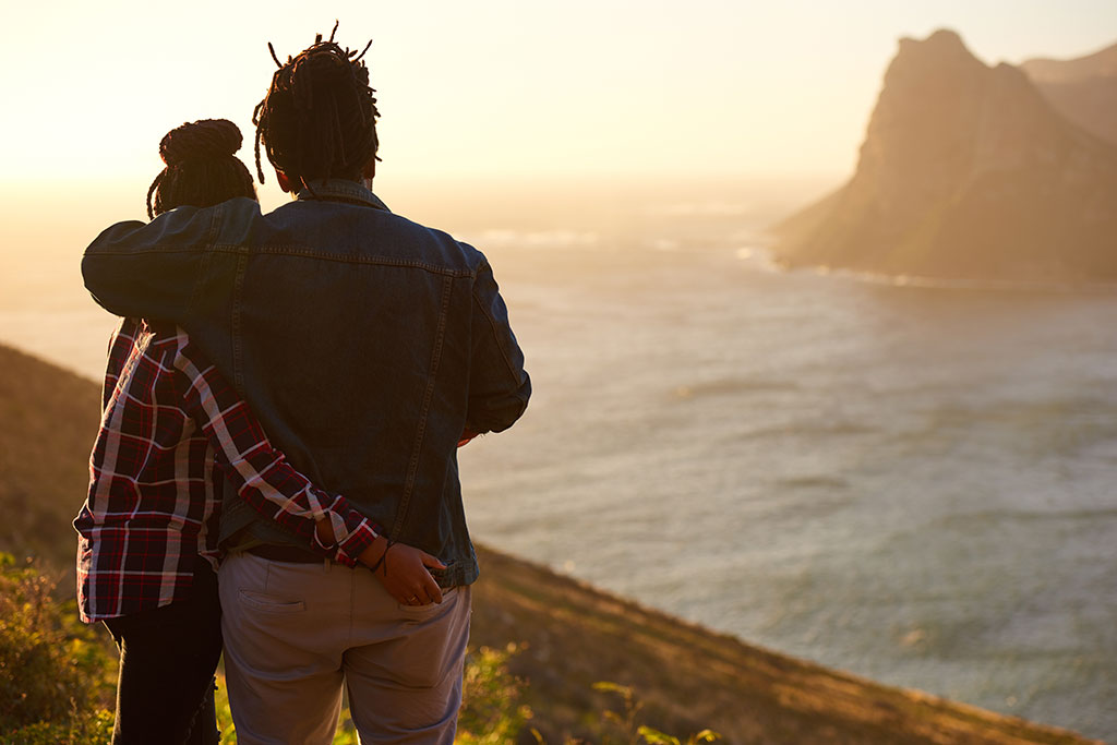A young couple standing together in the mountains and looking at the sea.
