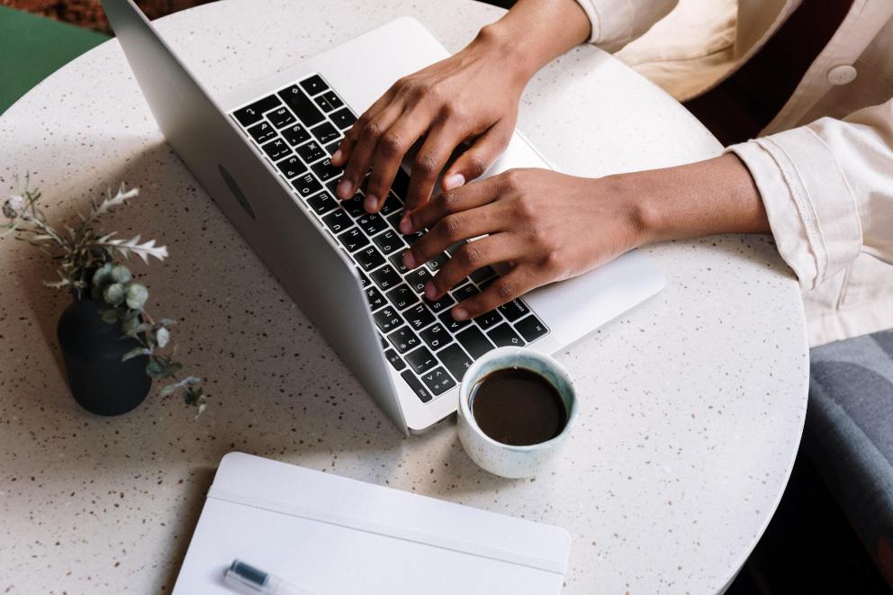 Woman seated at a table working on her laptop while she works out her budget and how much she can save each month. Next to her on the table is a mug of coffee.