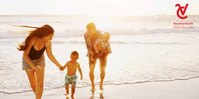 Mom and dad with their two children running on the beach with the sea in the background.