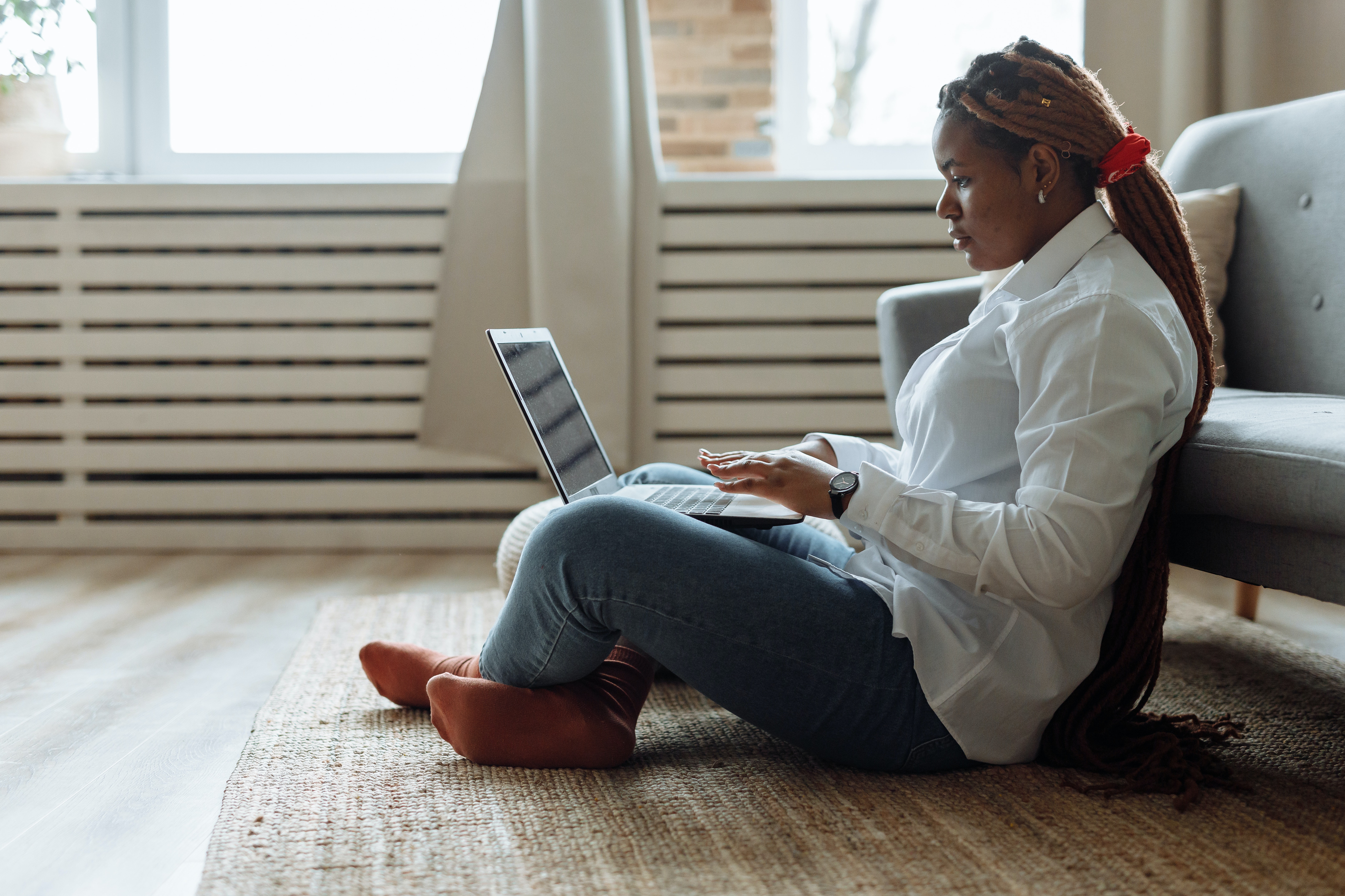 Young African lady seated on the floor working on her laptop.