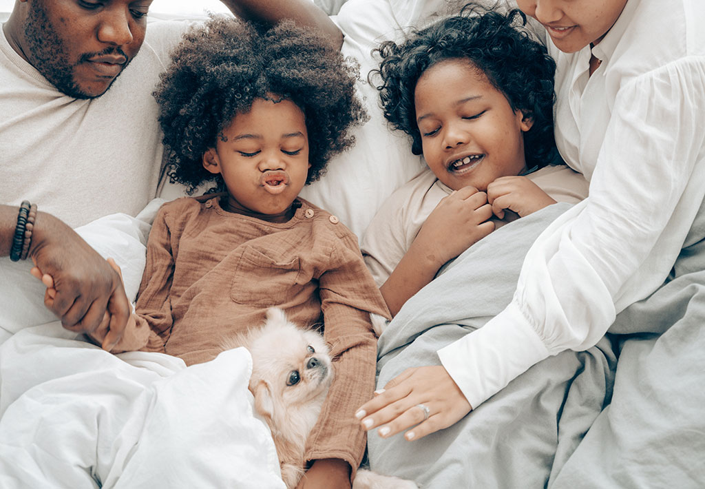 Mom, dad, 2 children and their dog lying on the bed together.