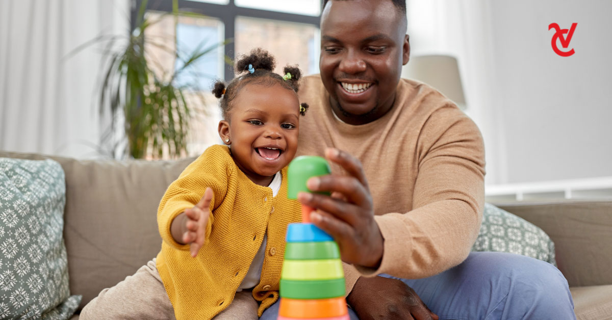 A dad and his young daughter are playing with an educational toy in their living room.