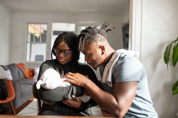 A young black couple sits together while the mom holds their small baby.