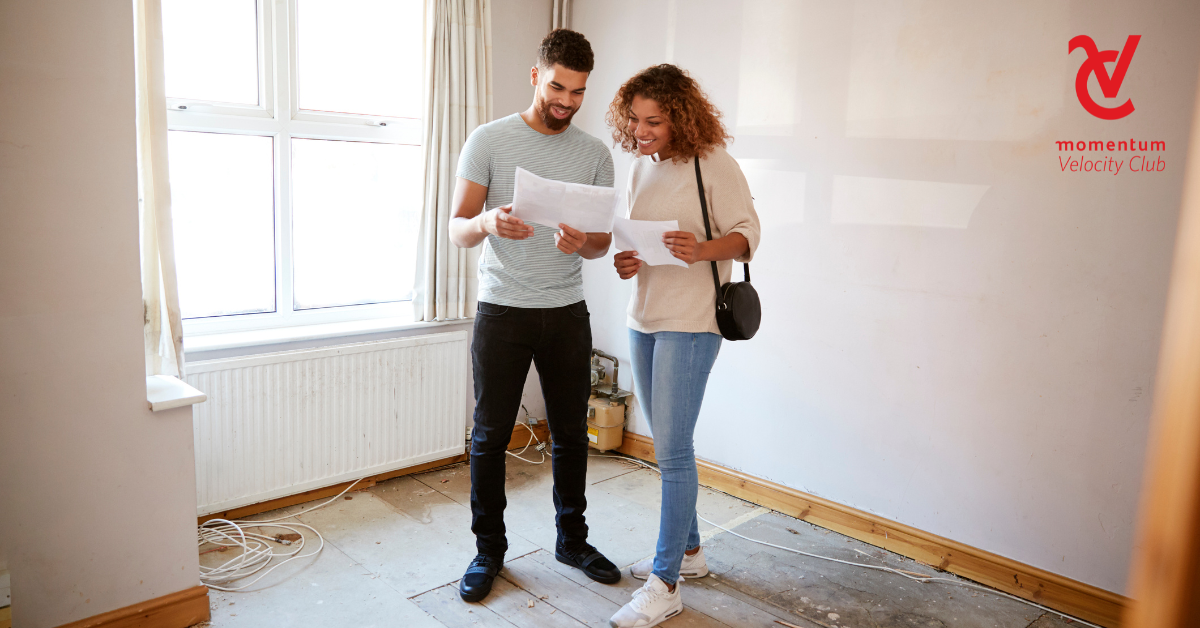 A young couple is standing in a home they're busy renovating. Each of them is holding papers and discussing their budget.