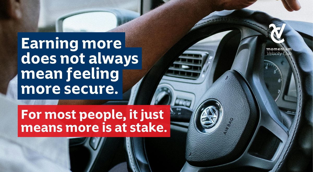 A close-up of a hand on a Volkswagen steering wheel, symbolising how earning more doesn’t always bring security, often, it just means more is at stake. Momentum Velocity Club logo is on the top right.