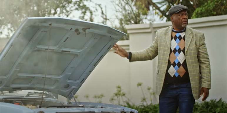 A retired man standing beside his overheated, broken-down car.