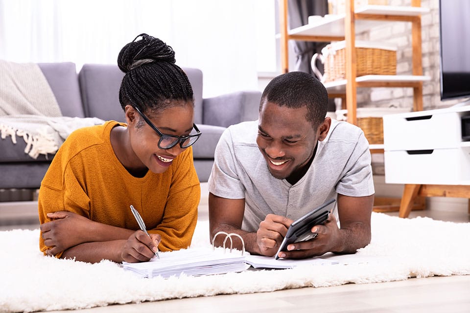 Young man and woman lying on their stomachs in their living room while they review their finances.