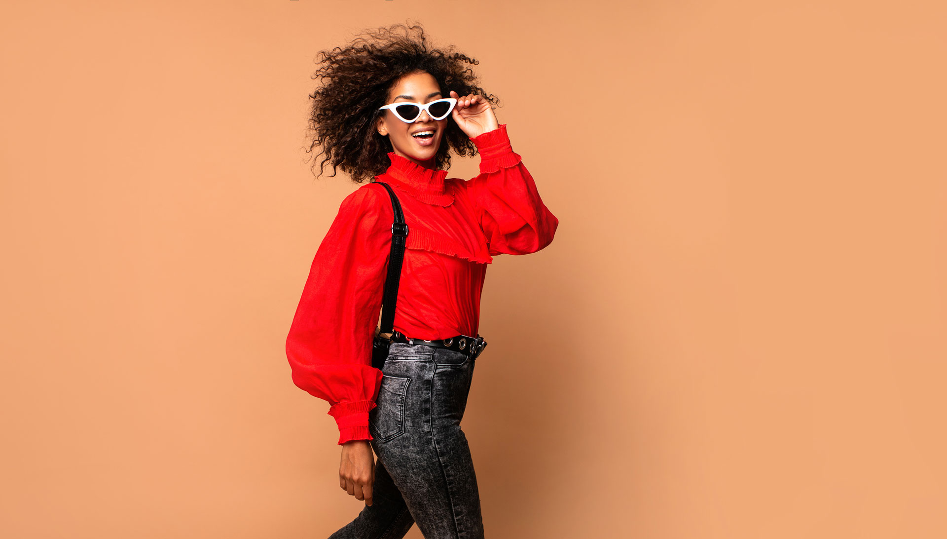 Financially confident young woman in red top and jeans putting on her sunglasses.