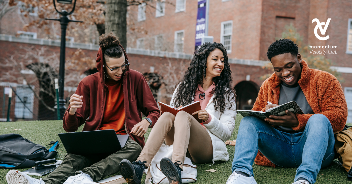 A group of university students is sitting on the grass outside, engaging in lively conversations and enjoying each other's company.